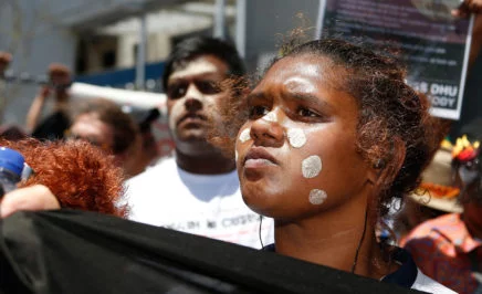 An Aboriginal woman holds a banner with other march participants behind her.