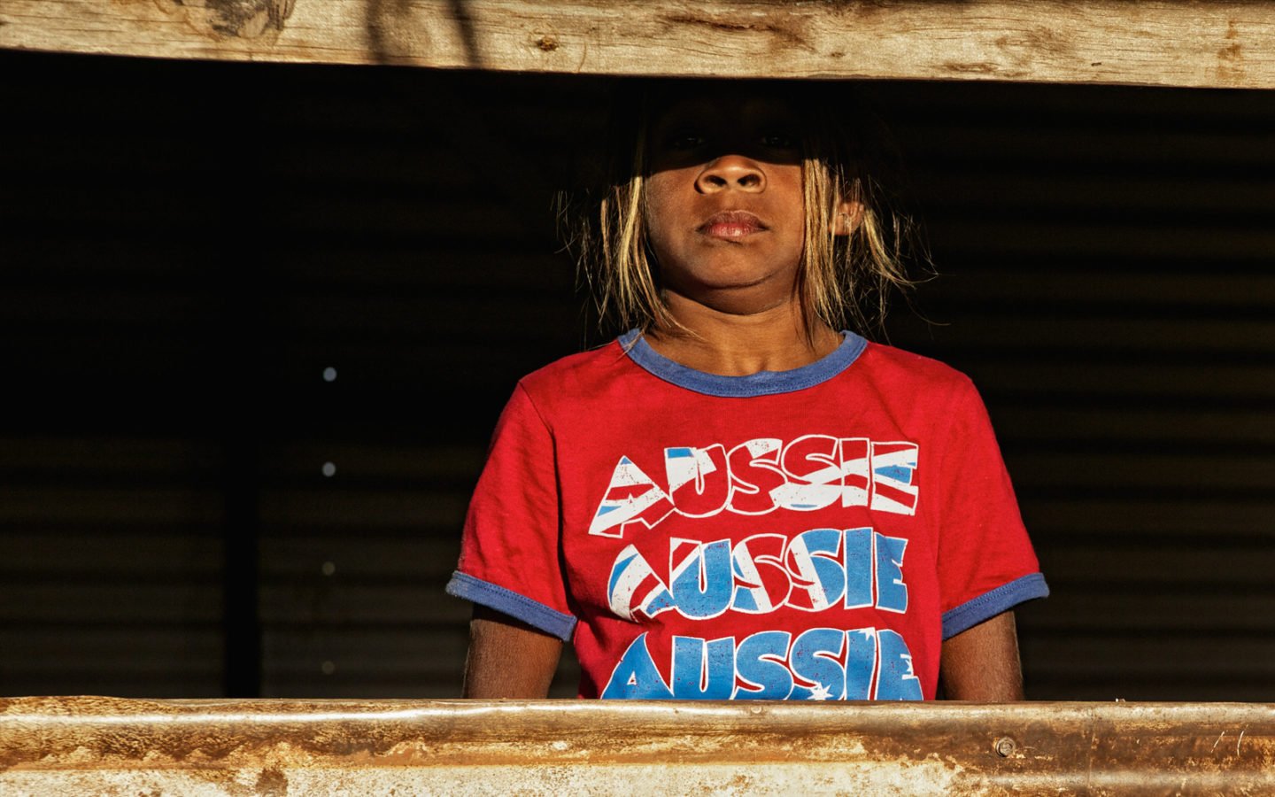 Aboriginal girl looking through old window, wearing a red t-shirt with 'Aussie' on it. Broome, Western Australia.