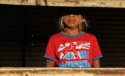 Aboriginal girl looking through old window, wearing a red t-shirt with 'Aussie' on it. Broome, Western Australia.