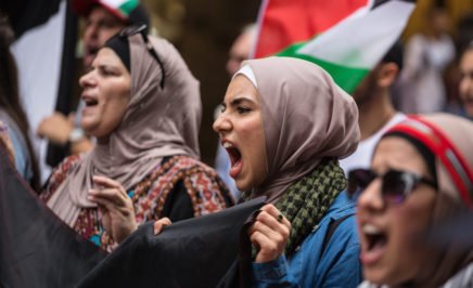 Women in Muslim and traditional Palestinian costume holding a banner and chanting slogans.