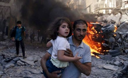 A man carries a young girl through rubble in Syria.