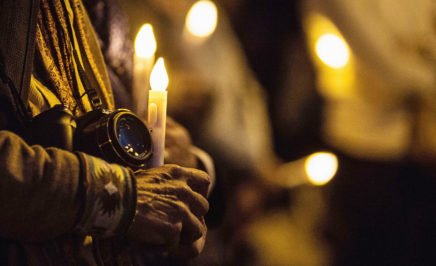 An activist holds a camera and a candle at a vigil