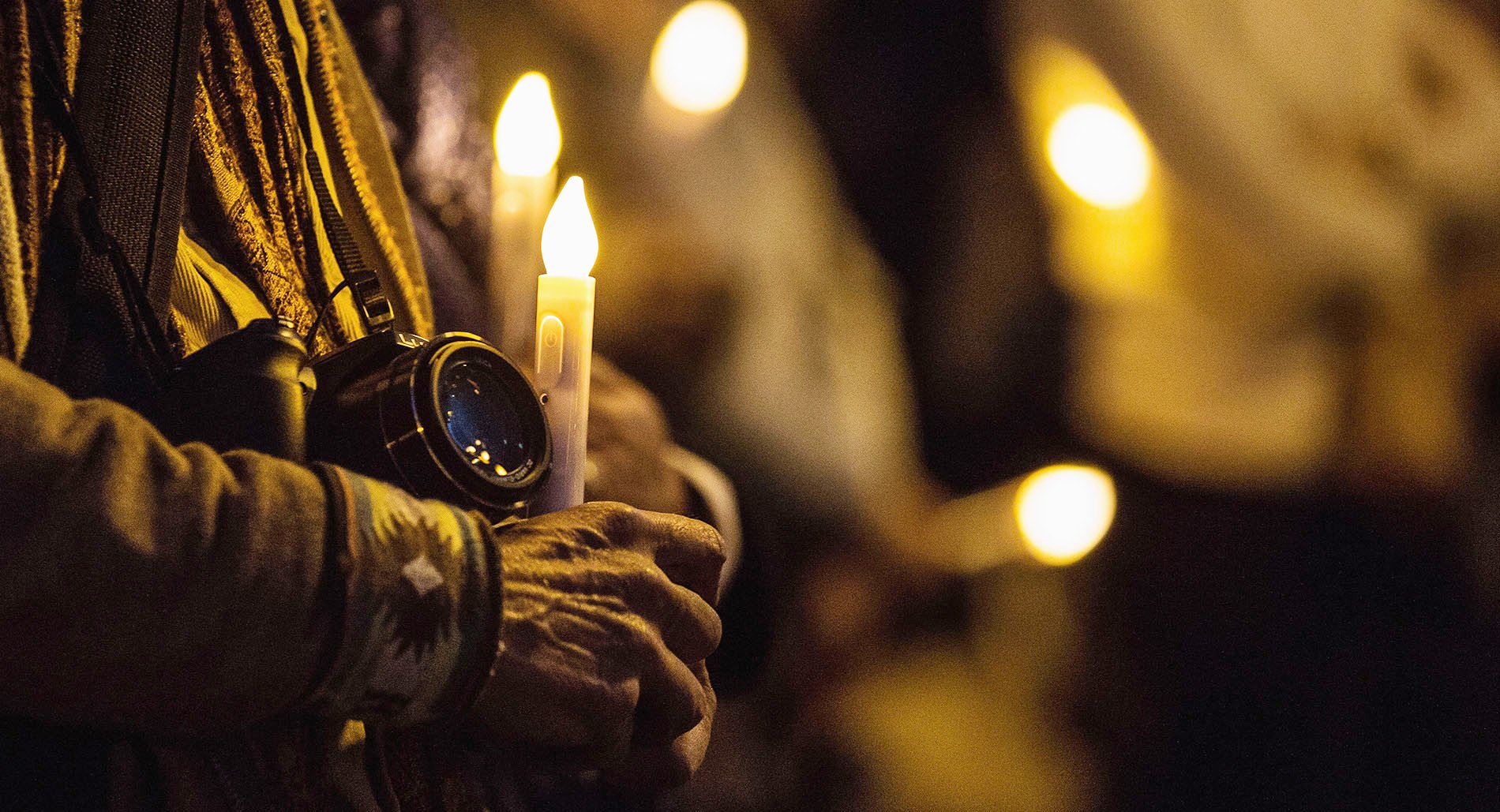 An activist holds a camera and a candle at a vigil