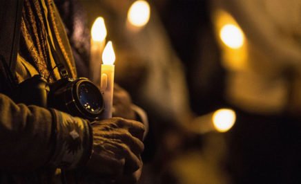 An activist holds a camera and a candle at a vigil