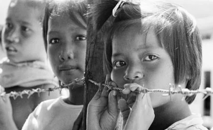 Three young refugees children leaning against barbed wire in South East Asia