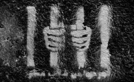 White graffiti of hands behind bars on a black wall