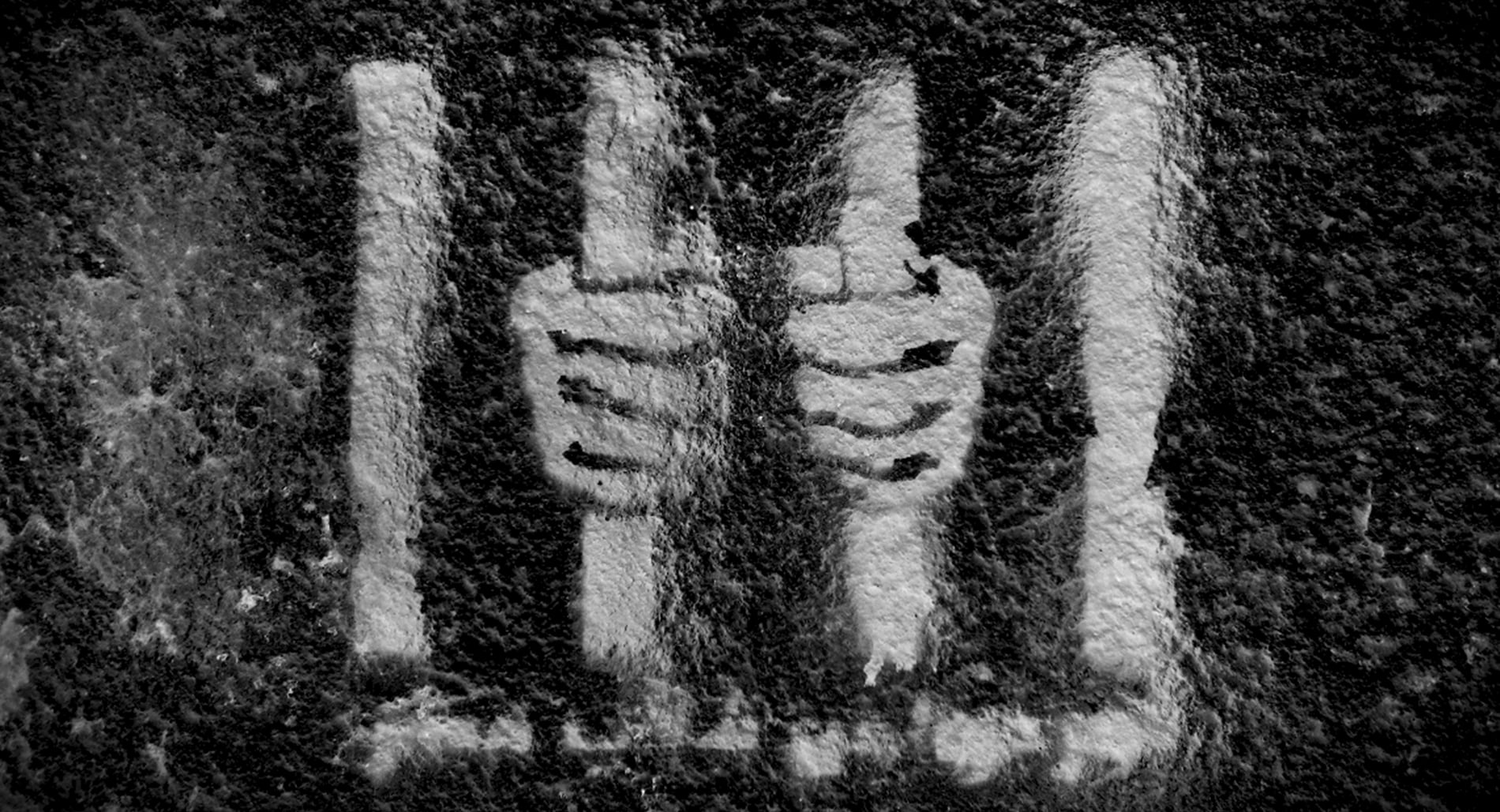 White graffiti of hands behind bars on a black wall