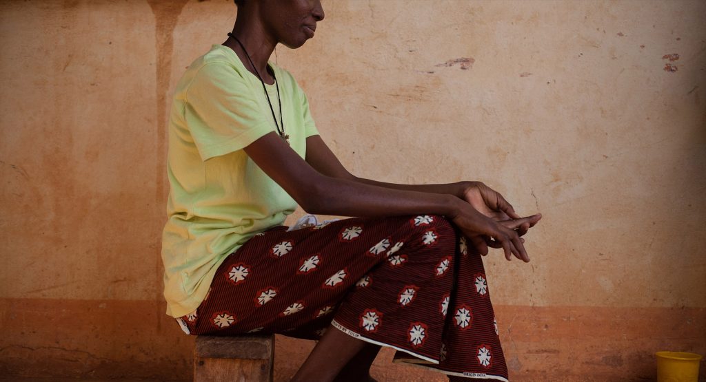 A woman seated on a wooden bench with a red skirt and her hands in her lap