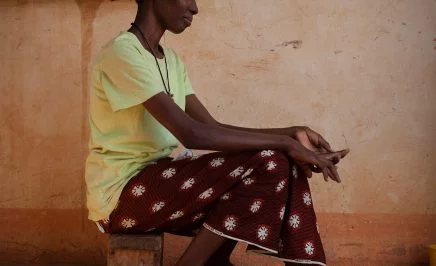 A woman seated on a wooden bench with a red skirt and her hands in her lap