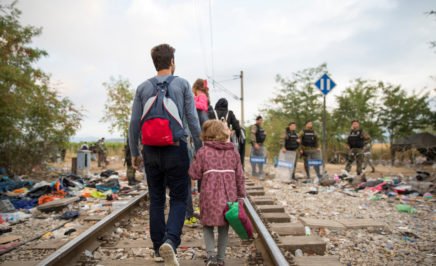 Refugees and migrants cross the border from Greece into Macedonia, A man with a backpack walks with a little girl along a train track.