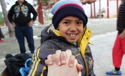 A young boy who is smiling - he is wearing a woolly hat and has his hand raised as he holds hands with the photographer.