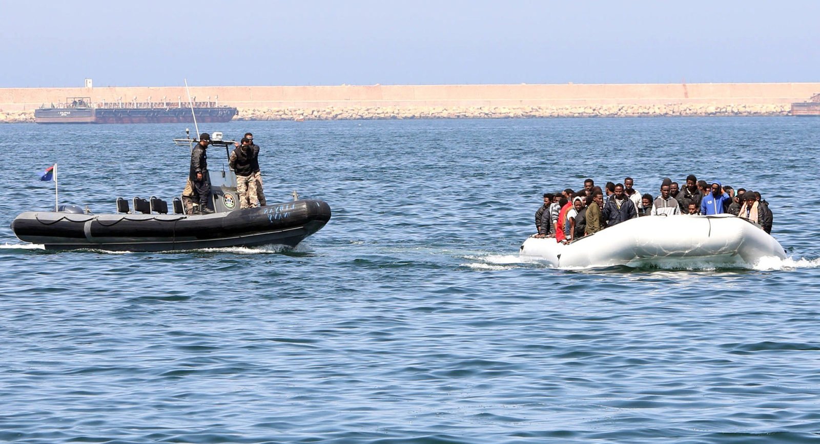 Libyan coast guards escort a boat along the coastline.