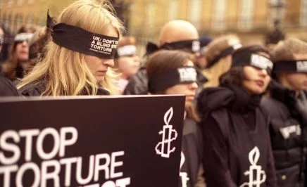 Activists at UK rally wearing 'Stope torture' shirts and blindfolds over their eyes.