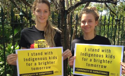 Two activists hold placards declaring that they stand with Indigenous kids for a brighter tomorrow
