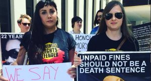 Two women holding signs stating "we say no to W.A mandatory sentencing laws" and "unpaid fines should not be a death sentence"