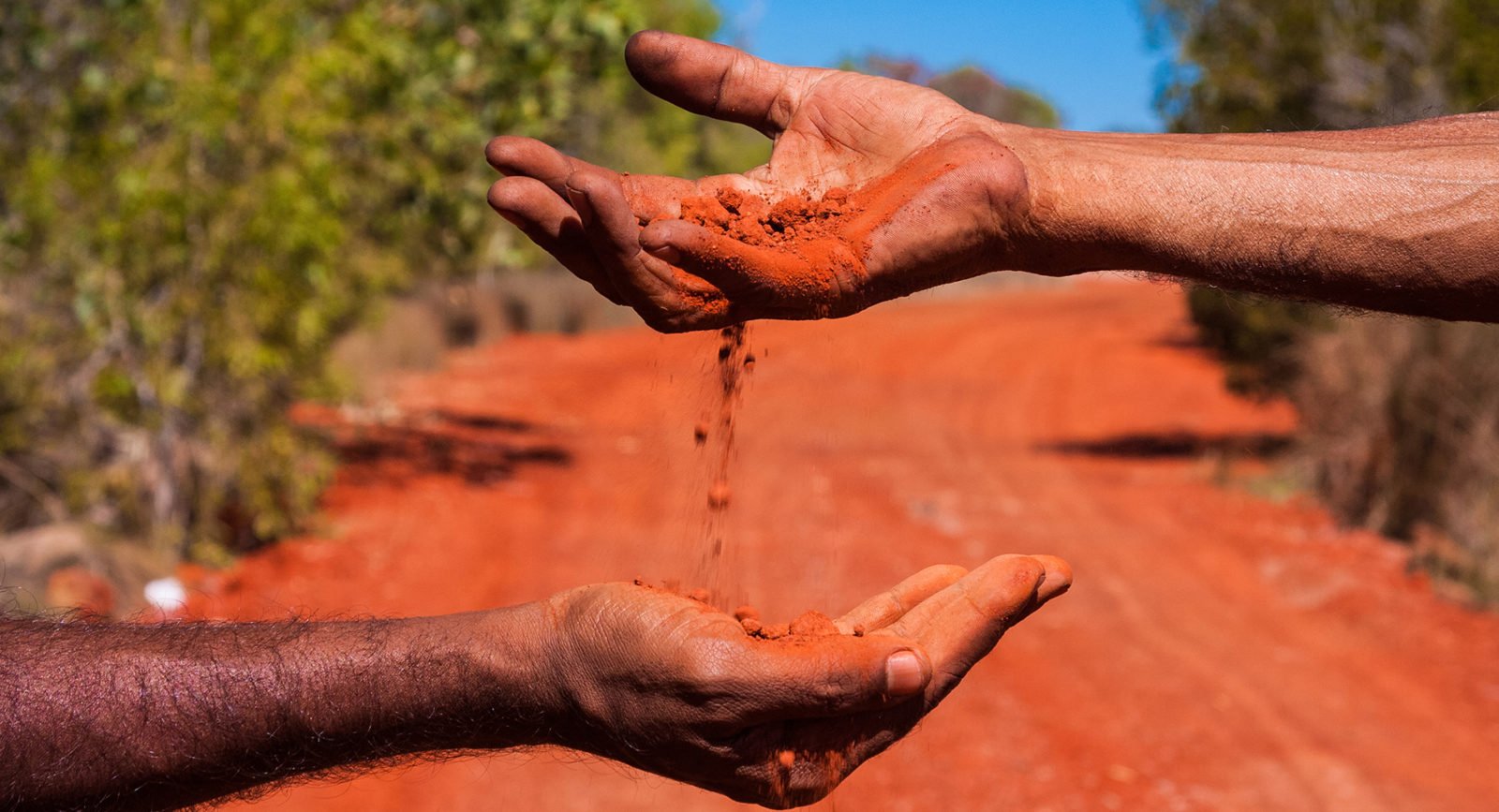 Red sand pouring through hands in the Australian desert