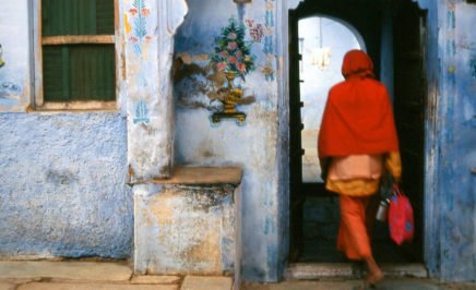 A person dressed in red walking through a blue doorway in India