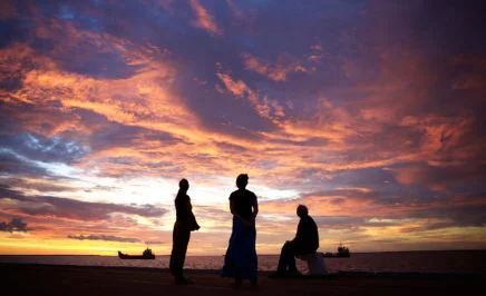 Three Indigenous people silhouetted at sunset by the ocean