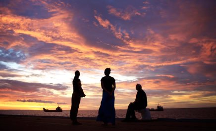 Three Indigenous people silhouetted at sunset by the ocean