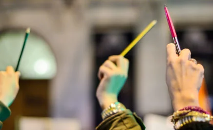 Three hands holding pens in the air.
