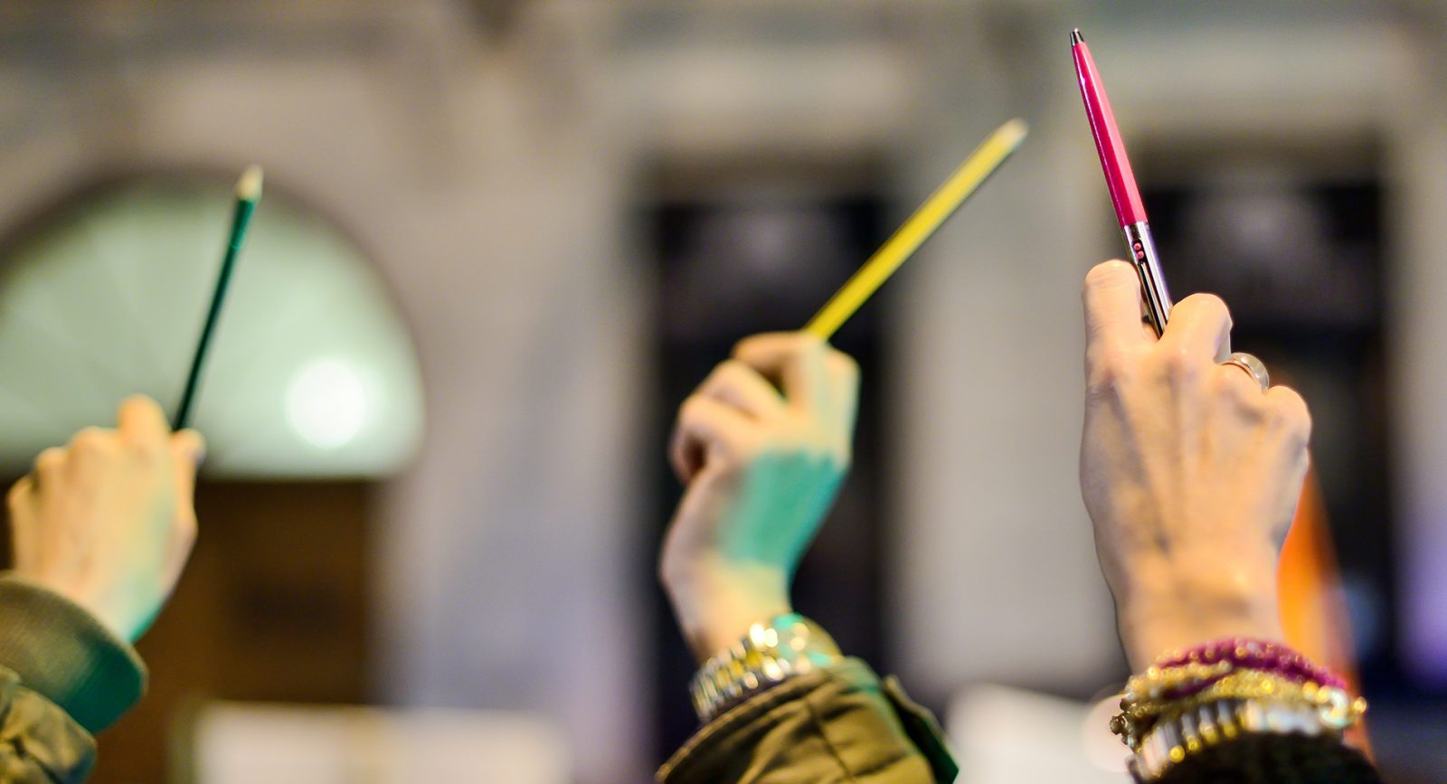 Three hands holding pens in the air.