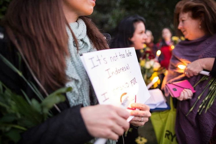 person holding a candle and sign saying 'it's not too late indonesia'