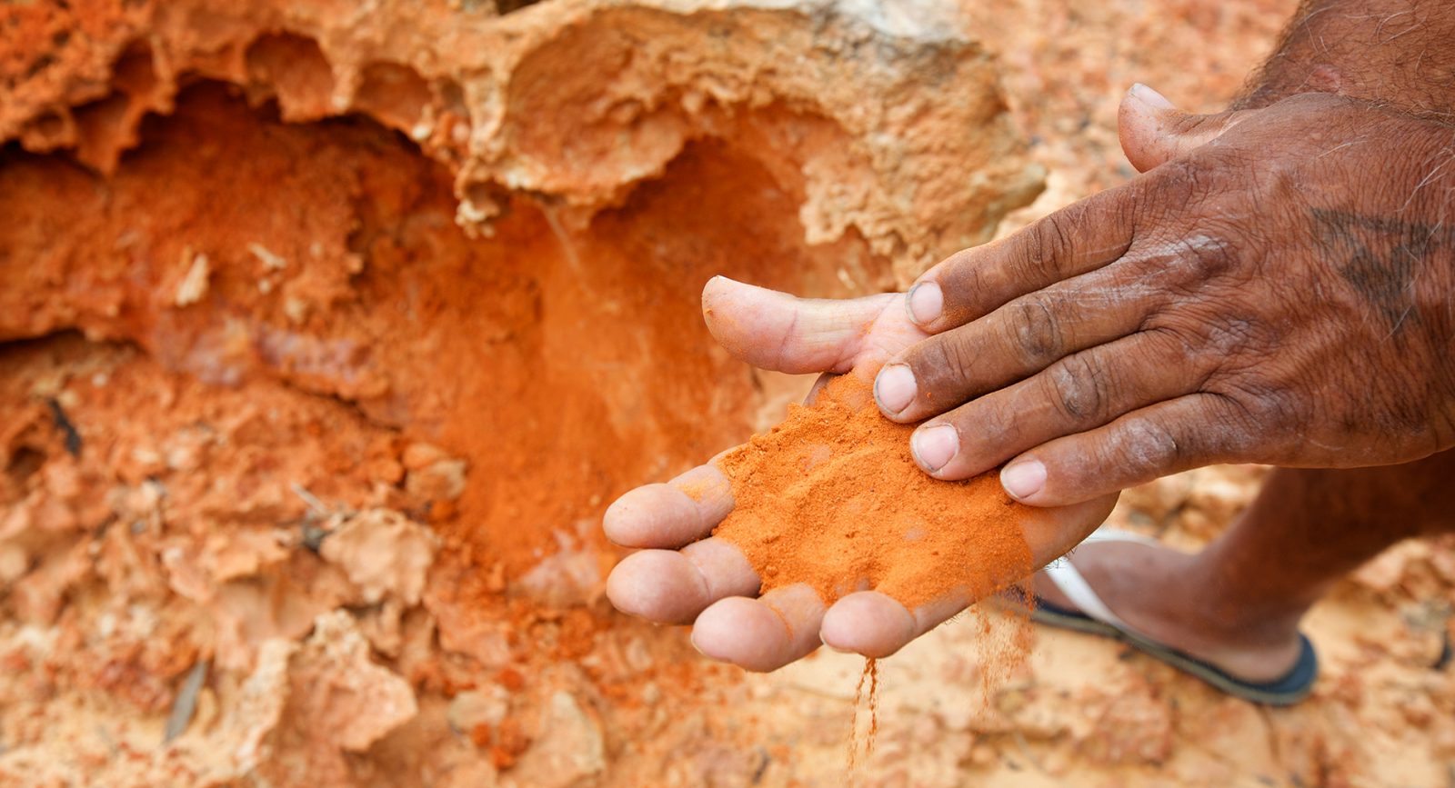 A pair of palms holding a handful of red sand at a red ochre site at Nowanup camp