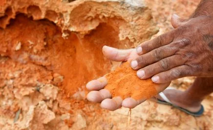A pair of palms holding a handful of red sand at a red ochre site at Nowanup camp