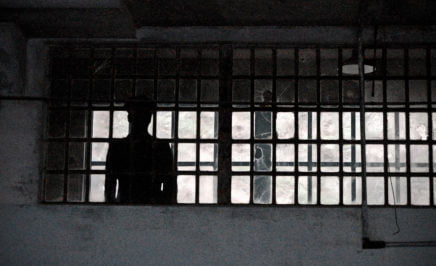 Silhouette of a prison guard standing behind bars
