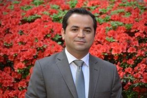 A man stands smiling with flowers in the background