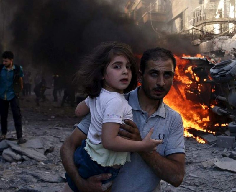 A man carries a young girl through rubble in Syria.