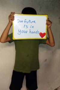 A child in the Refugee Processing Centre on Nauru holding a sign appealing for support. © Private