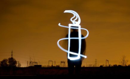 A light artist stands against a dark night sky and paints the AI candle.