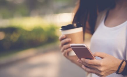 Close-up image of woman texting on her mobile phone and drinking coffee outdoors