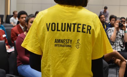 A photograph showing a volunteer wearing a yellow Amnesty t-shirt with the word 'Volunteer' writing across the back.