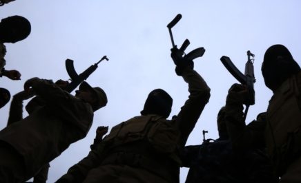 A group of men silhouetted against the sky hold up rifles in apparent celebration. The men are Iraqi police who have been training to retake the city of Mosul.