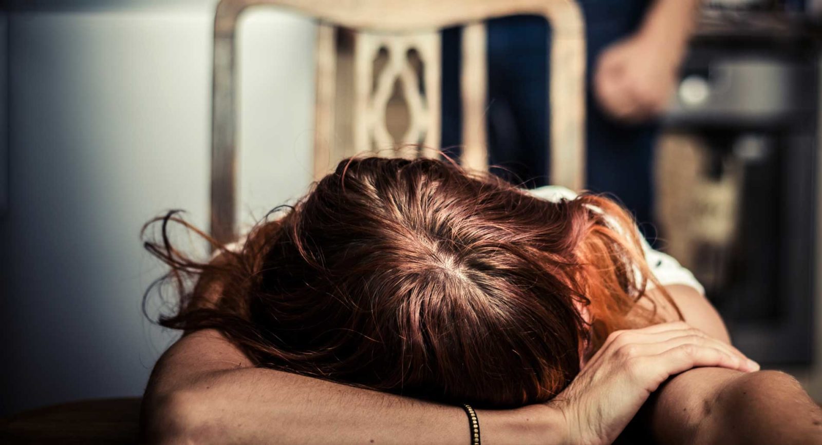 A woman with her head on a table and a man in the background