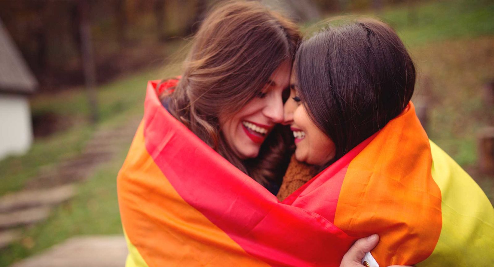 Two women embracing inside a rainbow flag