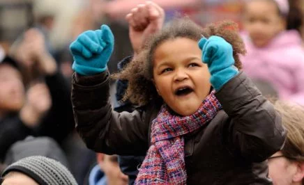 A girl with her fists in the air, on someon's shoulders in a protest