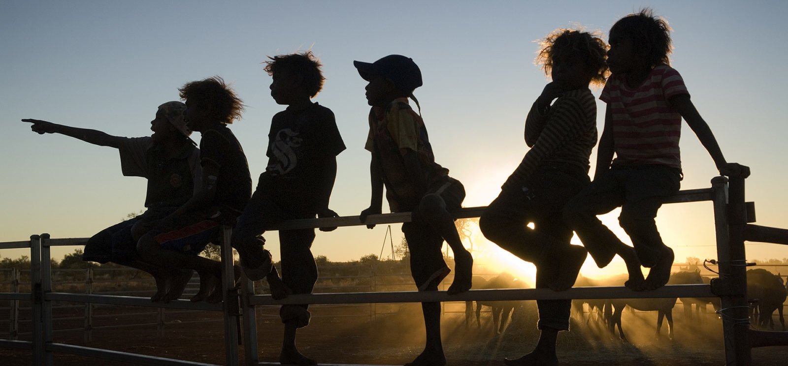 Silhouette of Indigenous children sitting on a fence