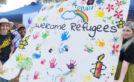 Three Amnesty activists holding a colourful banner that says Welcome Refugees.