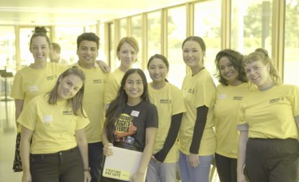 A group of volunteers wearing Amnesty yellow volunteer Tshirts & on in a black Indigenous Rights Tshirt are posed for the photo