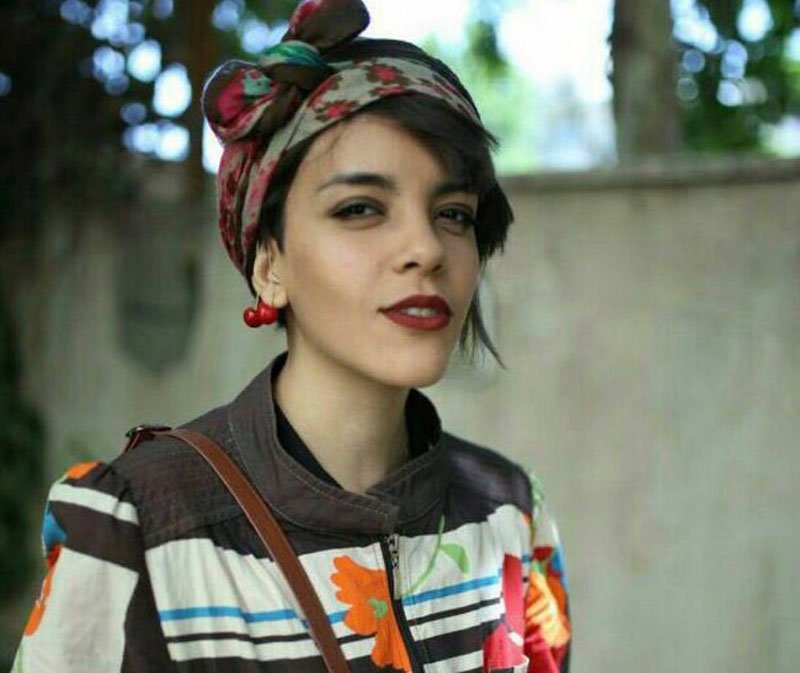 Iranian women's rights defender, Yasaman Aryani wearing a colourful head scarf and jacket in front of a grey wall.