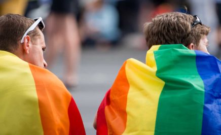 Two men wearing pride flags on their backs