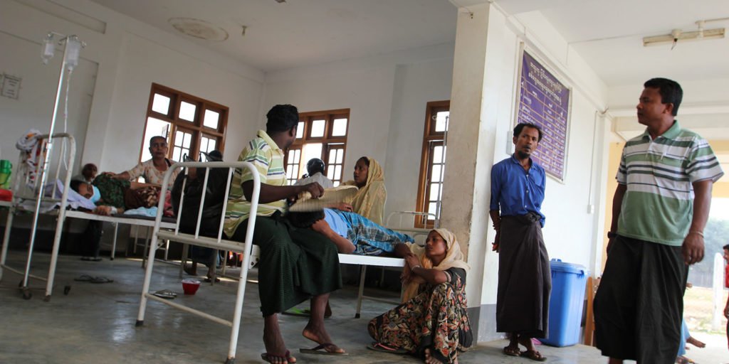 People inside a rudimentary clinic in a displacement camp in Sittwe town. Some people are looking at the camera, whilst others are in bed. 