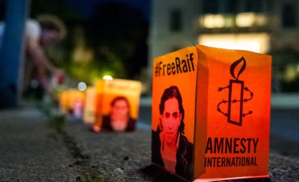 A row of paper candles with Raif Badawi's image printed on the side and the Amnesty International logo