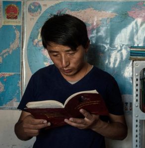 Tashi Wangchuk reading Tibetan text in front of world map
