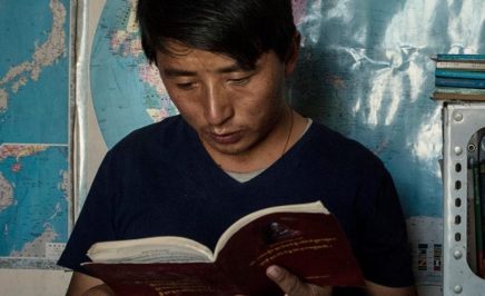 Tashi Wangchuk reading Tibetan text in front of world map