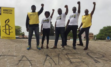 Five Amnesty activists (one woman, four men) stand in a line with their fists raised in solidarity with Taner Kılıç.