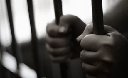 Two hands holding onto a set of prison bars in a jail cell